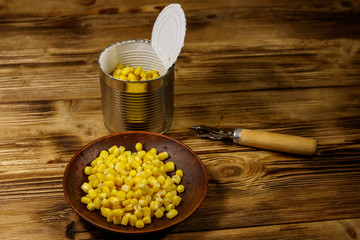 Open tin can and plate with corn and can opener on wooden table