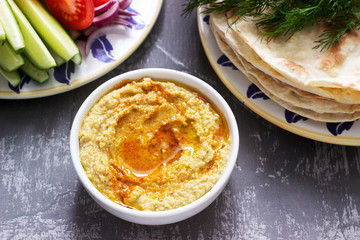 Vegan food, homemade hummus with flatbread, vegetables and olive oil on a concrete background.