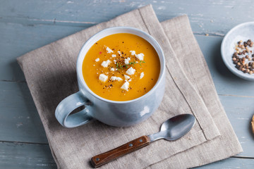 Spicy pumpkin and sweet potatoes soup in big ceramic mug garnished with feta cheese.
