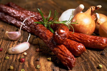 Smoked sausage on a wooden rustic table with the addition of fresh aromatic herbs and spices, natural product, produced by traditional methods - obrazy, fototapety, plakaty