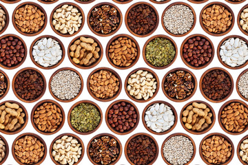 Raisins, cashews, apricot kernels, walnuts, sunflower seeds, hazelnuts, pumpkin seeds, peanuts and almonds in a wooden cedar bowl stand in rows on a white isolated background, top view. 