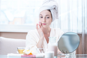 Beautiful young woman applying cream of natural cosmetics on face moisturizing the skin. Hygiene and care for the skin