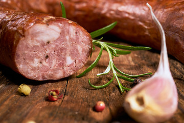 Smoked sausage on a wooden rustic table with the addition of fresh aromatic herbs and spices,...