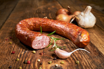 Smoked sausage on a wooden rustic table with the addition of fresh aromatic herbs and spices, natural product, produced by traditional methods - obrazy, fototapety, plakaty