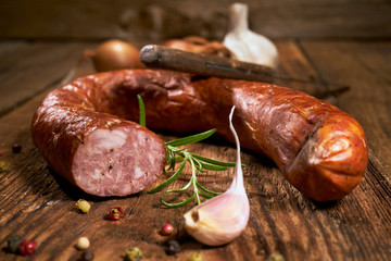 Smoked sausage on a wooden rustic table with the addition of fresh aromatic herbs and spices, natural product, produced by traditional methods