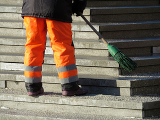 Street cleaning, municipal worker in uniform sweeping the stairs with a broom. Janitor in winter city, concept of unskilled labor