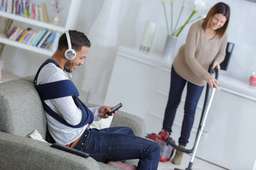 Obraz premium woman vacuuming while injured man is resting on a couch