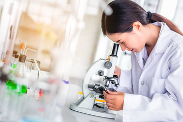Scientist sing microscope in laboratory with lab glassware containing chemical liquid, science or medical research and development concept 