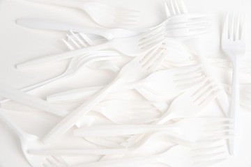 A bunch of disposable single-use white plastic forks set on a seamless white paper background.