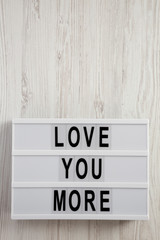 Modern board with text 'Love you more' on a white wooden background. Valentine's Day 14 February. Copy space.