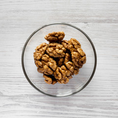 Walnuts in glass bowl on a white wooden surface, overhead view. Closeup. Flat lay, from above, top view.