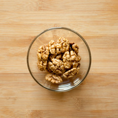 Walnuts in glass bowl on bamboo surface, top view. Flat lay, overhead, from above.