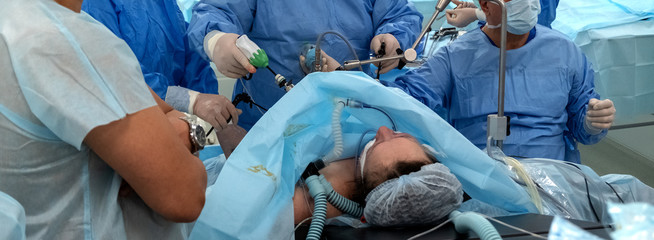 Panorama. Endoscopy. Operating room in the hospital. Surgical table. A team of surgeons using endo-instruments operate the patient's abdomen. Surgery on the body of a full woman. Endovideosurgery.