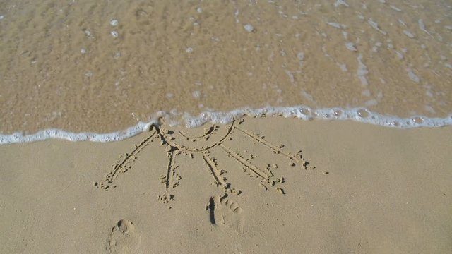Sun drawn on sand. The drawing of the sun on the sand is washed away by the wave.