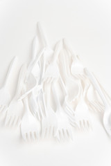 A bunch of disposable single-use white plastic forks set on a seamless white paper background.