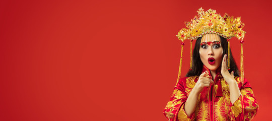 Chinese traditional graceful woman at studio over red background. Beautiful girl wearing national costume. Chinese New Year, elegance, grace, performer, performance, dance, actress, dress concept