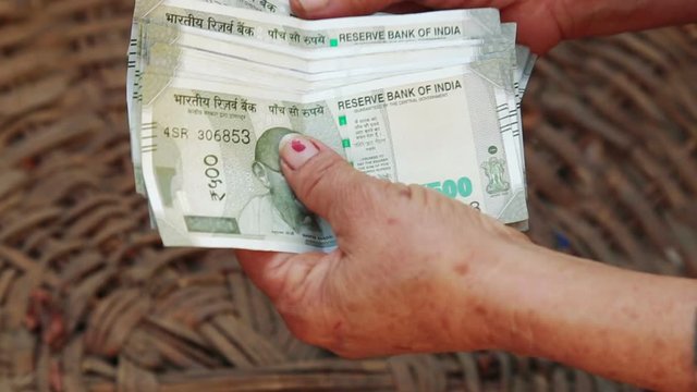 Close up of Poor elderly Indian/Asian woman counting five hundred paper Indian money rupees over her empty vegetable basket. concept of making money in Agriculture