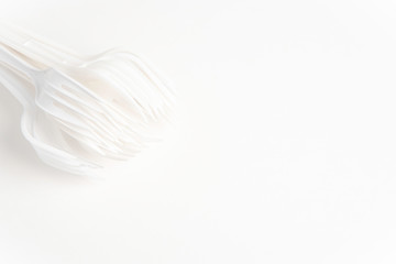 A bunch of disposable single-use white plastic forks set on a seamless white paper background.
