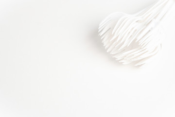 A bunch of disposable single-use white plastic forks set on a seamless white paper background.