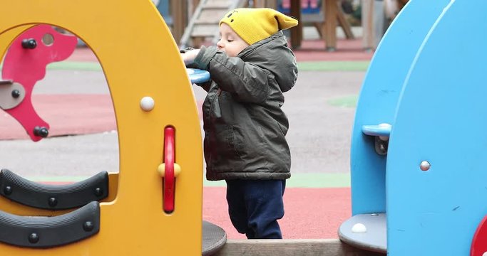 Cute Baby Boy With A Funny Yellow Hat And A Winter Jacket At The Outdoor Playground. Close Up Portrait View - DCi 4K Resolution