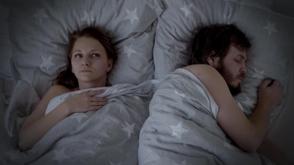 Man Snoring in Bed, Woman cannot sleep. Husband snoring, his Wife is Waking up, troubled sleep. Spouses are Sleeping in bedroom at Night.