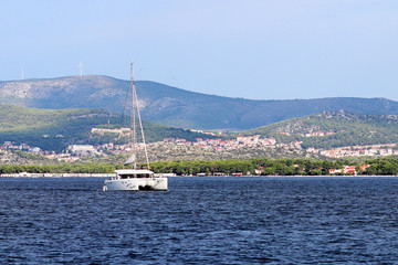 Sailing catamaran sails along the rocky green coast past the red literary sign - the fairway...