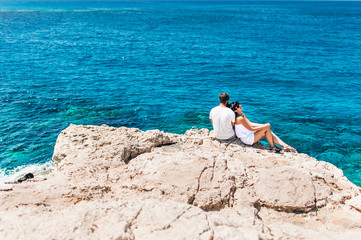 Couple in love by the sea on the rock. Honeymoon lovers. Man and woman traveling. Couple in love on vacation. Newly married couple. Sea tour. Honeymoon trip. The couple on the cliff by the sea