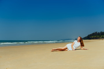 Fototapeta na wymiar Fashion shot of a beautiful girl in a white dress lying on the beach. Goa India