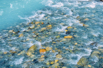 Beautiful ripples on river flow over colorful stones in summer sunshine, Siberia, Altai Republic