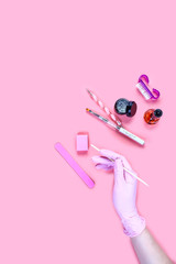 manicure and pedicure equipment. master nails in pink gloves holds manicure tool on the pink background. flat lay composition for card with a place for text. vertical image