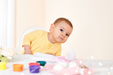 Baby girl sitting at the table and painting holiday easter eggs smiling happy childhood concept