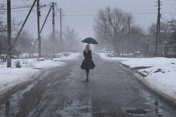 Girl with an umbrella is on the road in winter.
