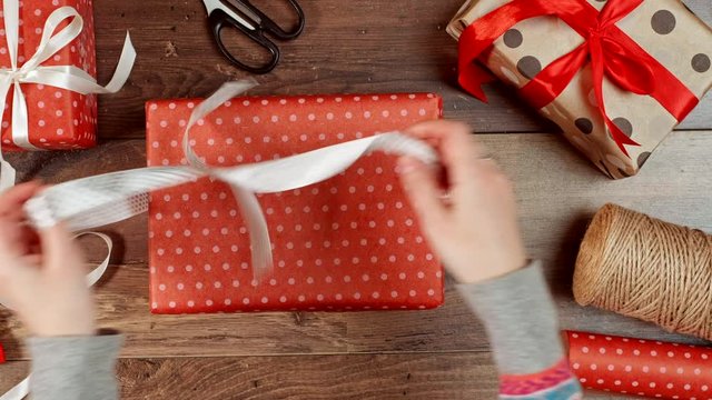 Person hands unpacking present on wooden background with paper. Woman opening wrapped red gift box with ribbon and bow. Birthday, anniversary, Valentine's, Christmas holidays packaging.