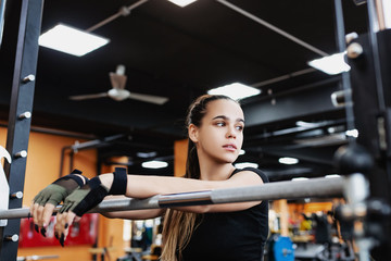 Portrait of a beautiful young posing fit girl standing near the bar preparing for the exercise. Concept of strong-willed and trained professional athlete