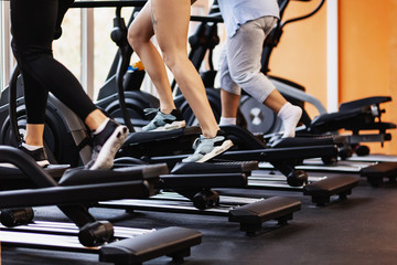 Attractive young people working out on an elliptical trainer in gym. The concept of volitional discipline and endurance. - obrazy, fototapety, plakaty