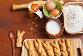 Homemade freshly baked Easter cookies for children in the form of bunnies and the products for it cooking: flour, sugar, eggs and vegetable oil on a wooden table. Flatlay style