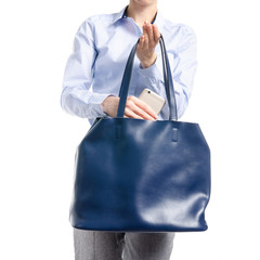 Woman in gray pants and blue shirt put smartphone in blue bag macro on white background isolation
