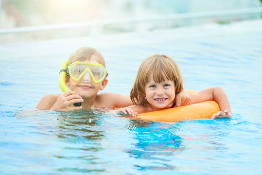 Cheerful brothers spending summer day in swimming pool with inflatable ring and snorkel