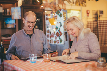 Senior couple giving a look to menu in typical Italian restaurant - Valentine’s Day celebration, love and dating concept.