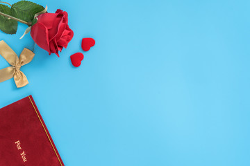 Red greeting card with golden bow at Valentine's day, anniversary, mother's day and birthday for a surprise on blue background, copy space, top view