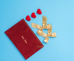 Red greeting card with golden bow at Valentine's day, anniversary, mother's day and birthday for a surprise on blue background, copy space, top view