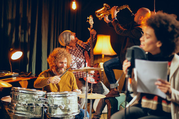 Mixed race woman singing. In background band playing instruments. Home studio interior. Selective focus on band.