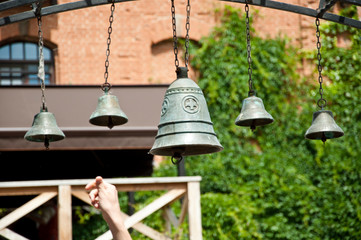 Obraz premium The art of ringing a set of tuned bells. Church bells hanging outdoor. Bells ringing on wind. Metal bells on metallic chains hung on arc in church yard. Calling to christian mass or worship service