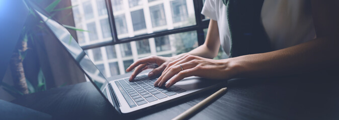 Woman working on laptop keyboard at the office wile sitting at the table. Wide