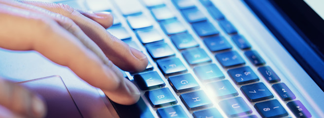 Closeup of male hands typing on laptop keyboard at the office. Visual effects, flares. Wide