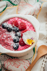 Berry Acia bowl topped with blue berries, raspberries, desiccated coconut, chia berry yogurt and edible white pansy flower on vintage embroided tea towl and wooden spoons