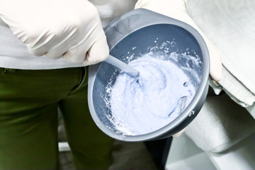 Cosmetologist in white gloves in beauty salon stirring Caviar peel off mask for facial skin care in plastic bowl with plastic stick, preparation for skin treatment, close up 