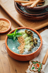Spirulina Acia bowl with toppings of candied pumpkin seeds, kiwi fruit, bee pollen and fresh mint, on a brown wooden background