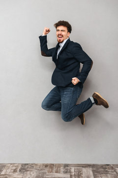 Handsome emotional young business man isolated over grey wall background jumping.
