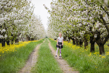 Little blonde girl skating in blooming apple and cherry garden. Warm springtime and mothers and woman day